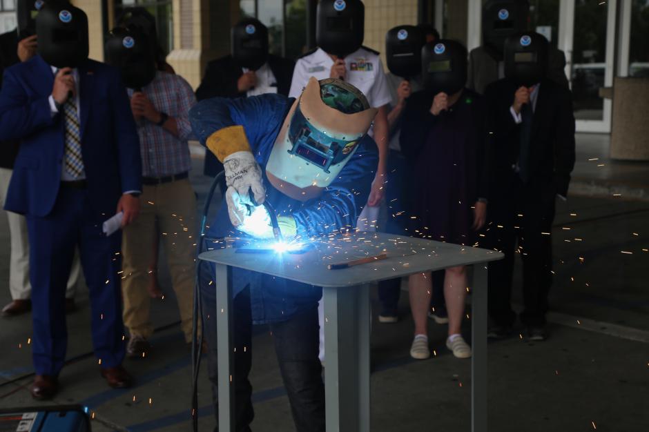 A welder working on a metal plate while a group of people look on