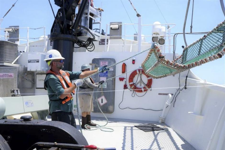 Two crew members aboard a white NOAA ship pull in a mesh cradle