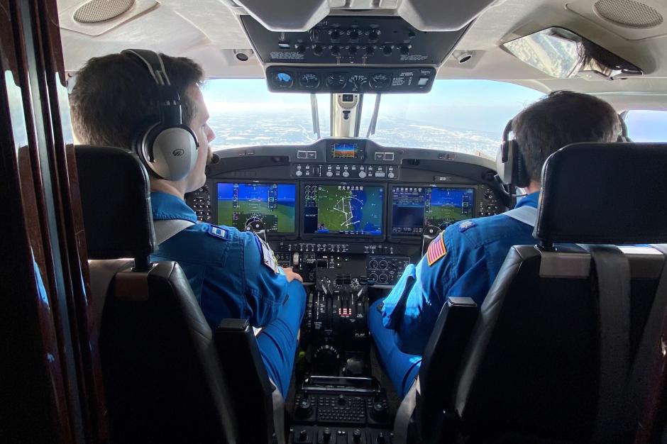 Two pilots in blue flight suits at the controls of a NOAA King Air aircraft