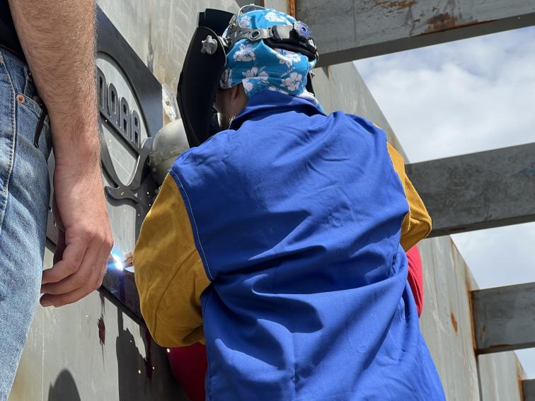 RDML Amanda Goeller welds NOAA plaque onto pier
