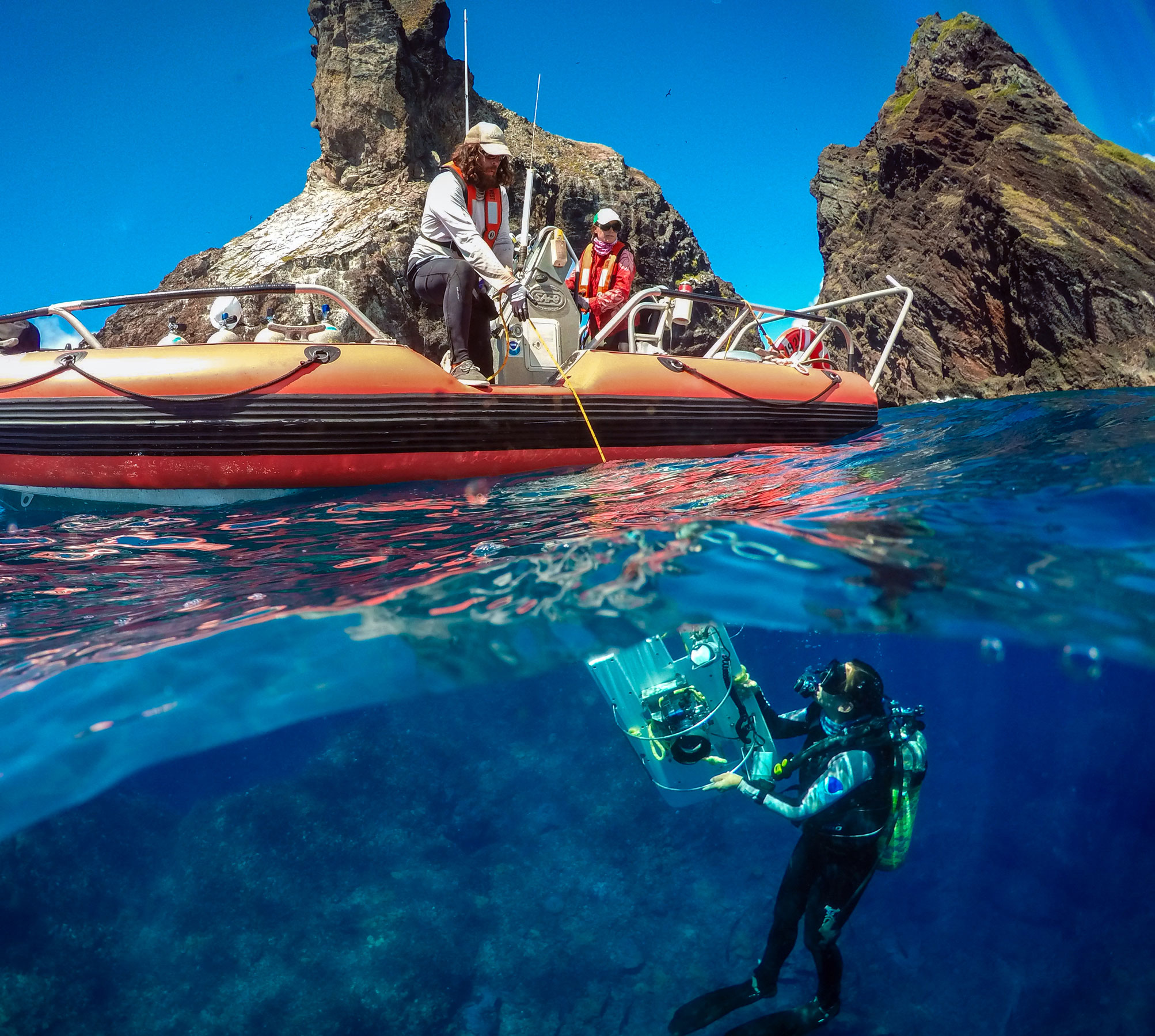 Two people in a small boat help a diver bring up a towboard
