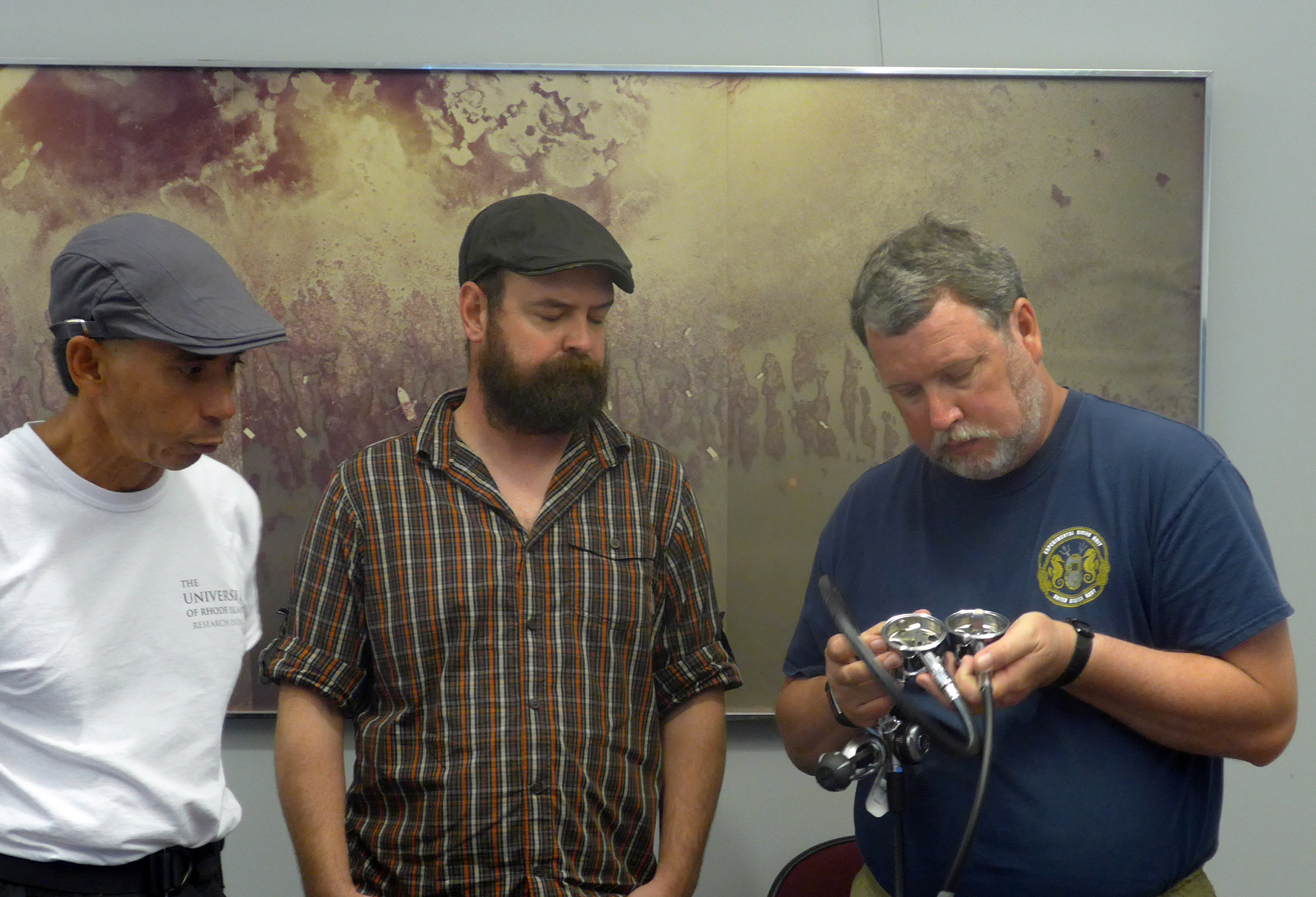 Three men examining the inside of a SCUBA regulator