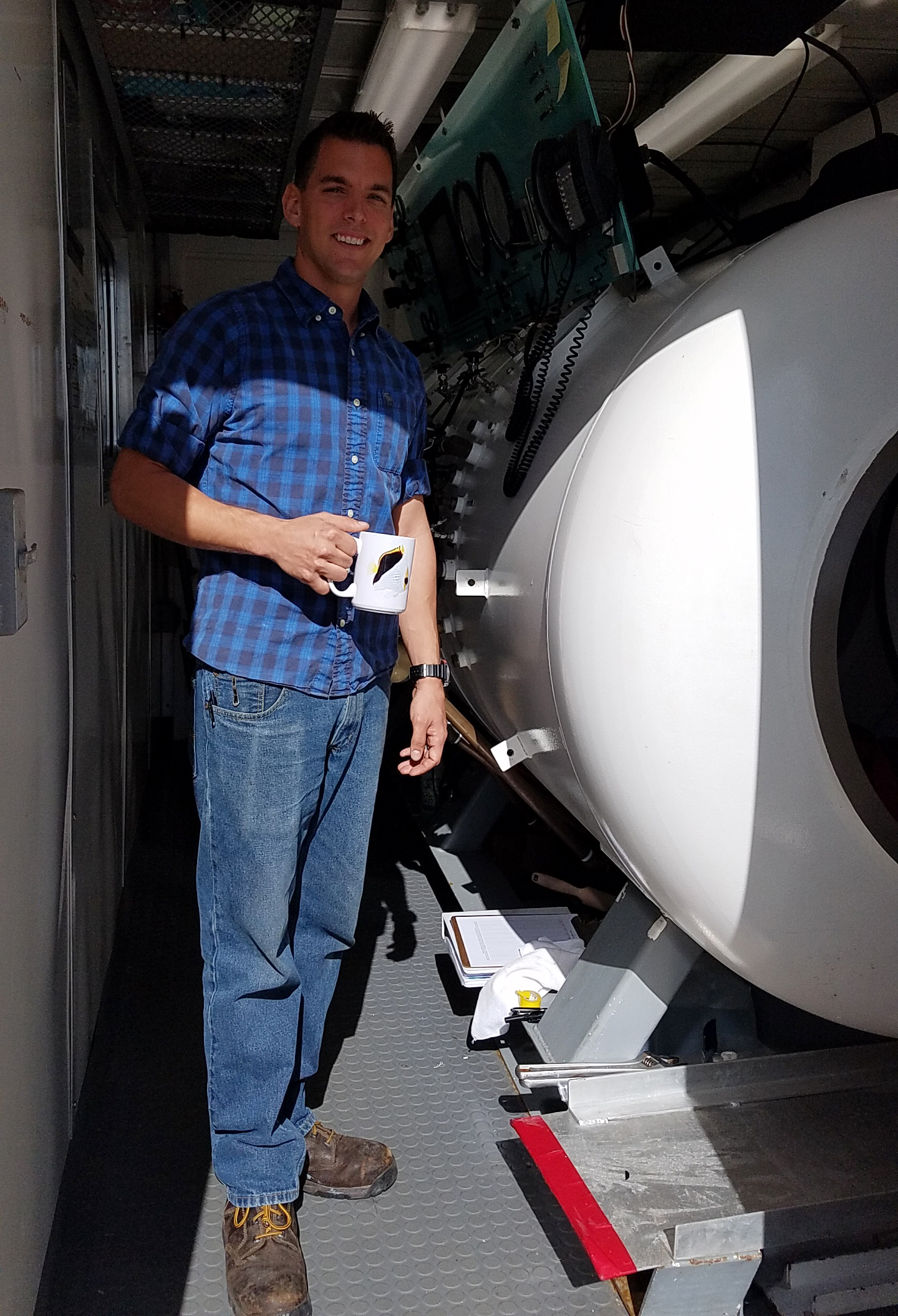 A diving medical technician stands next to a hyperbaric chamber