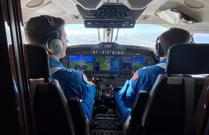 Two pilots in blue flight suits at the controls of a NOAA King Air aircraft