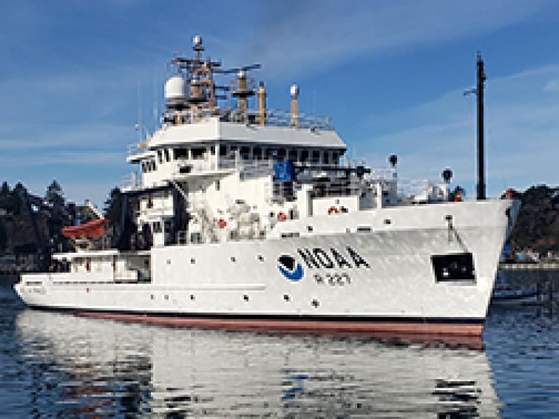 A white NOAA fisheries survey ship under a blue sky