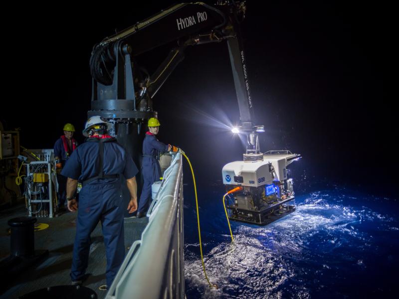 A robot submarine dangling from a ship's crane at night