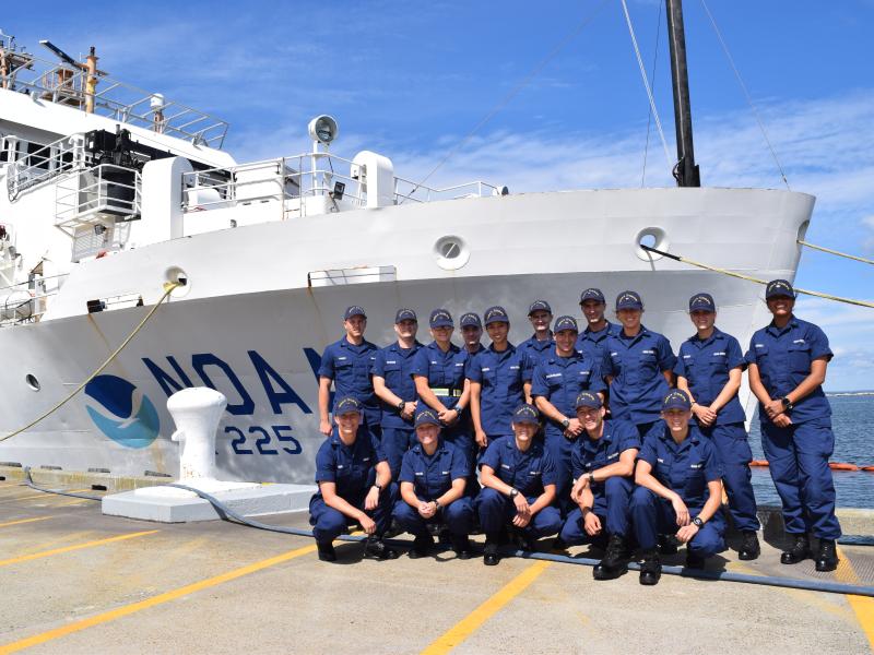 NOAA Corps officer candidates clad in blue uniforms on the pier in front of a white NOAA ship