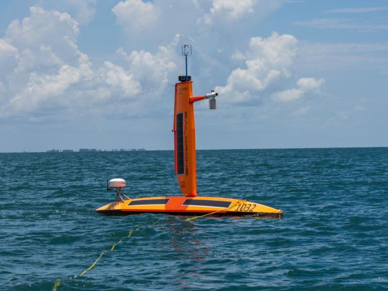 A bright orange uncrewed Saildrone surface vehicle on the water