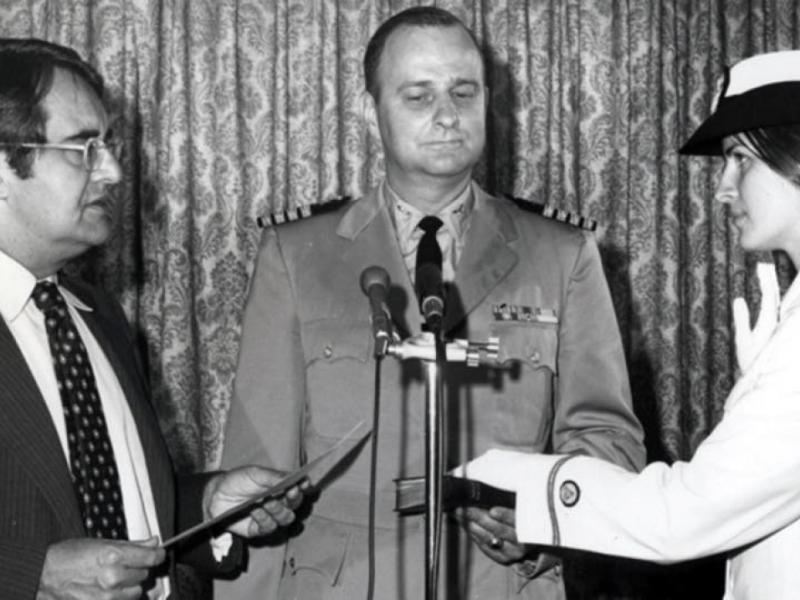 A black-and-white photograph of Ensign Pamela Chelgren was sworn in by Secretary of Commerce Peter G. Peterson on July 6, 1972. Her father, Navy Captain John Chelgren is in the center holding the Bible