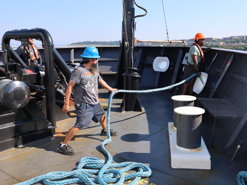 Two crew members handle mooring lines at a ship's bow