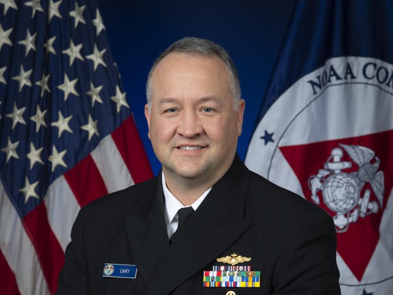 Rear Admiral Chad Cary with U.S. and NOAA Corps flags behind him