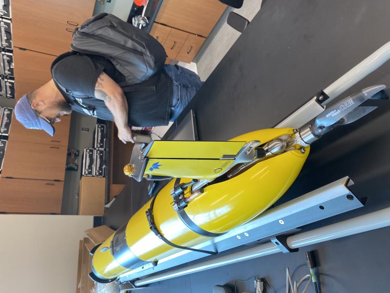 A NOAA employee stands next to a yellow glider on a lab bench.