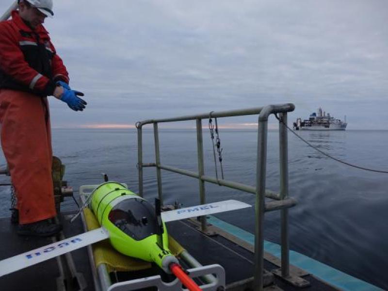 A glider technician prepares to launch the Oculus glider from a platform. A ship is visible in the distance.