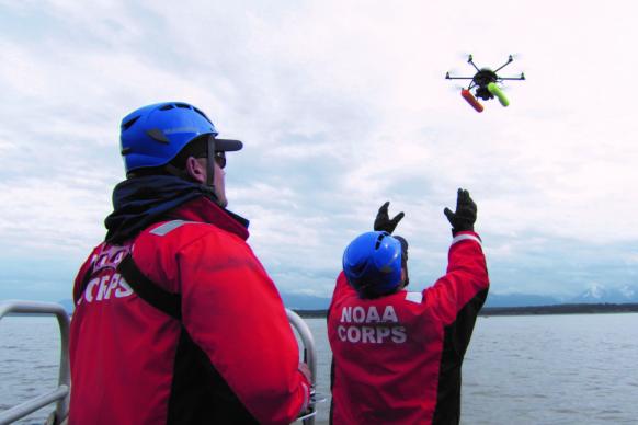 Two NOAA Corps officers launch a hexacopter drone into the air