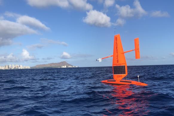 A bright orange Saildrone uncrewed surface vehicle on the water