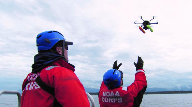 Two NOAA Corps officers launch a hexacopter drone into the air