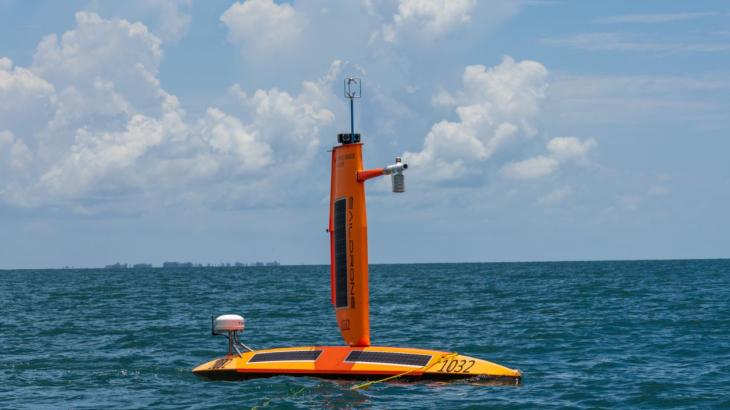 A bright orange uncrewed Saildrone surface vehicle on the water