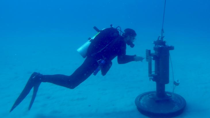 A NOAA diver inspects a piece of equipment on the sea floor.