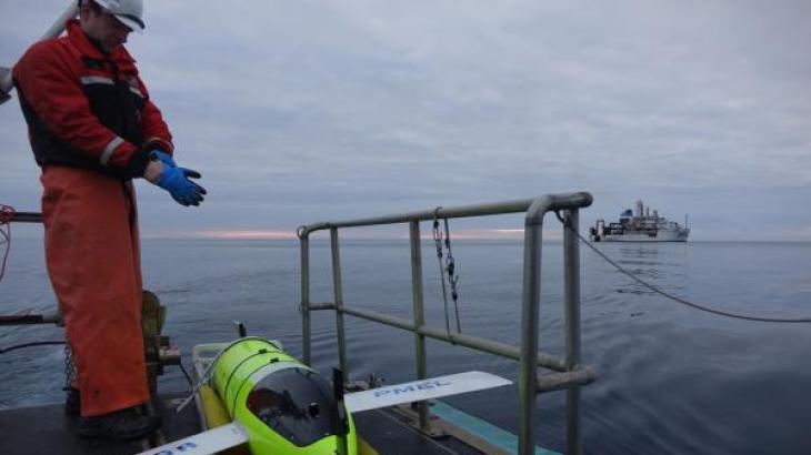 A glider technician prepares to launch the Oculus glider from a platform. A ship is visible in the distance.