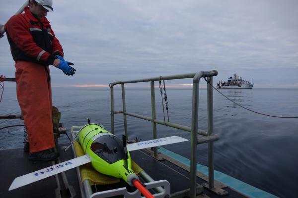 A glider technician prepares to launch the Oculus glider from a platform. A ship is visible in the distance.